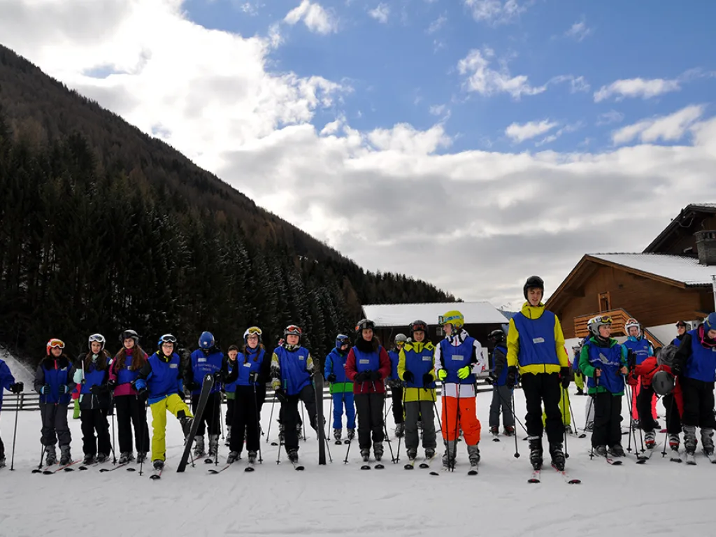 Gruppe in blauen Leibchen steht auf Skiern am Hangfuß.